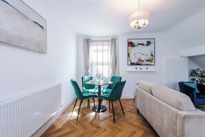 Uma sala de estar moderna com uma mesa redonda de vidro, cadeiras verde-água, um sofá bege, uma lareira e uma grande pintura abstrata.