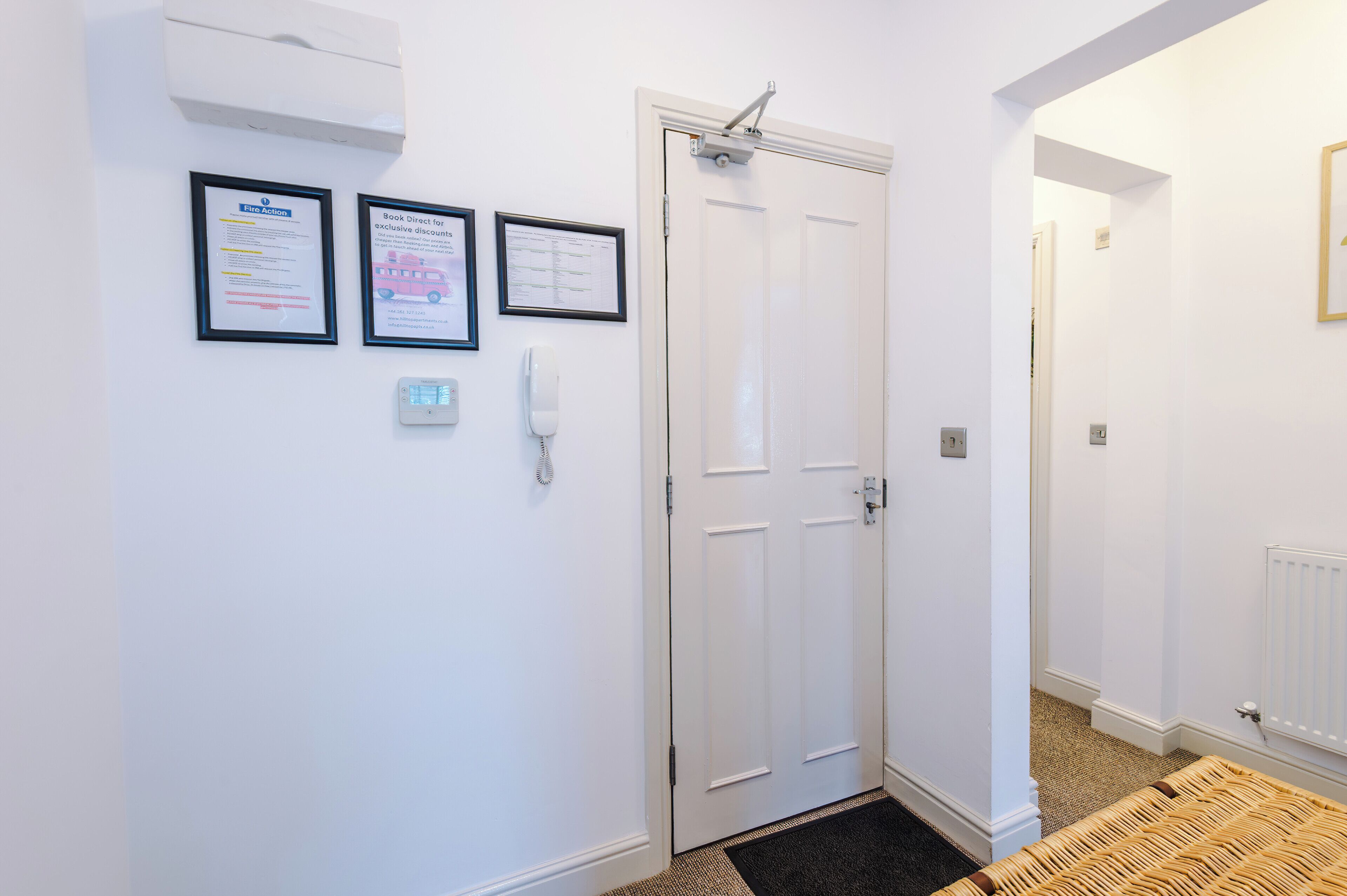 A hotel entrance with a white door, a wall-mounted intercom, and two framed notices.