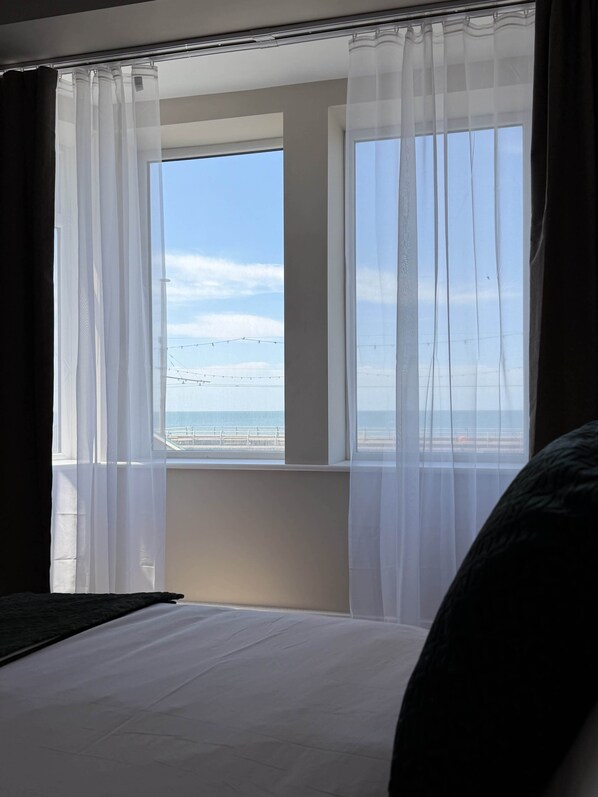 A hotel room with a large window, a bed, and a view of the beach. - Emerald Tide Hotel (Blackpool)