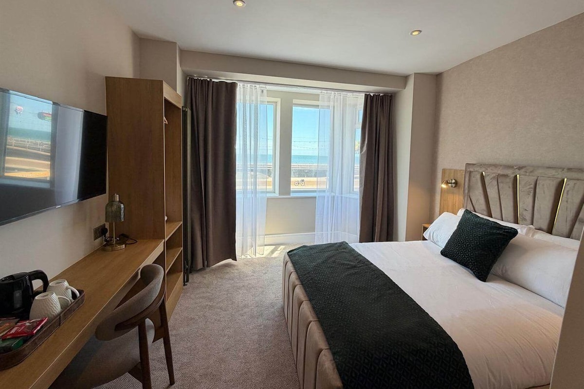 A hotel room with a bed, a desk, a chair, a television, and a window with curtains.