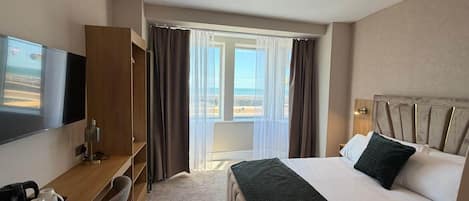 Habitación de hotel con cama, escritorio, silla, televisor y ventana con cortinas.