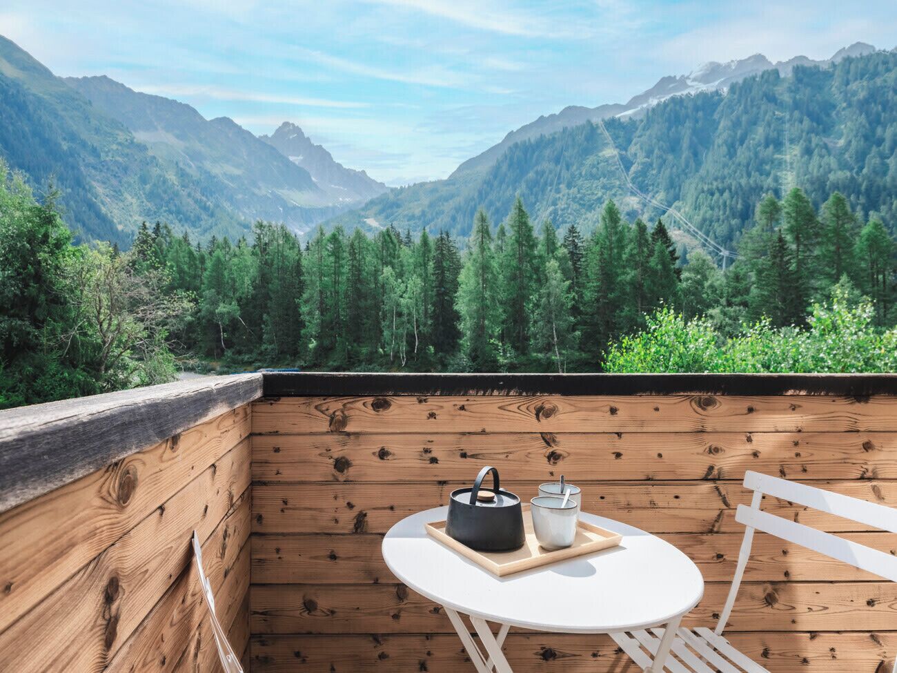 A wooden deck with a table and chairs, overlooking a mountainous landscape.