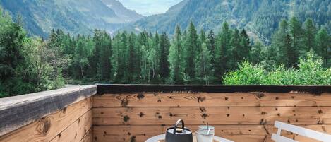 Une terrasse en bois avec une table et des chaises, offrant une vue sur un paysage montagneux.