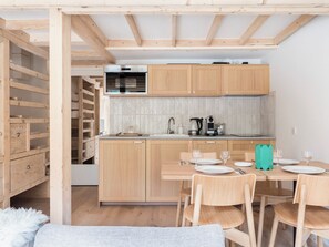 A compact kitchen with wooden cabinets, a dining table set for four, and a staircase leading to an upper level. - Renovated duplex with a balcony and parking space (Chamonix-Mont-Blanc)