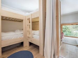 A room with two bunk beds, a window with a view of trees, and a blue rug on the floor. - Renovated duplex with a balcony and parking space (Chamonix-Mont-Blanc)
