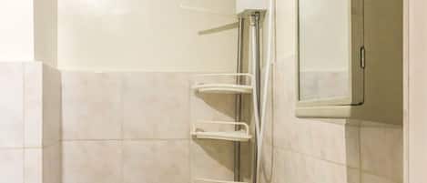 Un baño con lavamanos blanco, un espejo, ducha con cabezal de ducha manual y un desatascador azul.
