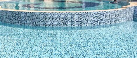 A swimming pool with a tiled edge, surrounded by multi-story residential buildings.