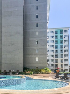 A swimming pool with a tiled edge, surrounded by lounge chairs and a small garden area.