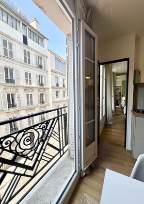 Ein Balkon mit Blick auf ein Gebäude, eine Tür, die in einen Innenraum führt, und ein Einblick in eine Küchenzeile.