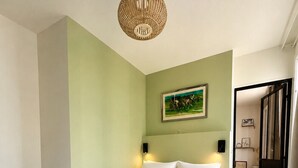 A bedroom with a large bed, a wall-mounted light fixture, and a painting. - Montmartre, Place du Tertre · Quiet & Bright (Paris)