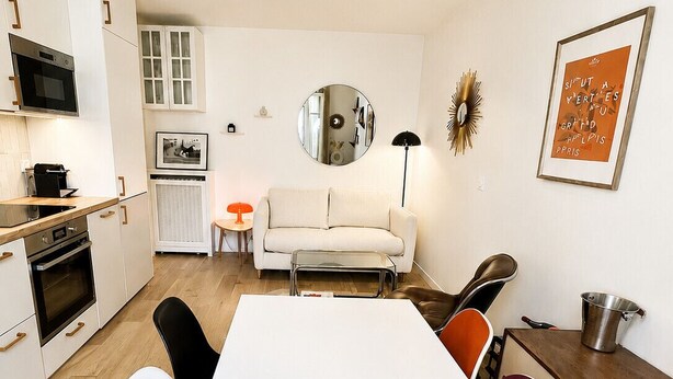 A modern kitchen with white cabinets, a dining table with chairs, a sofa, and a chandelier. - Montmartre, Place du Tertre · Quiet & Bright (Paris)