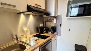 Uma cozinha compacta com uma pia de aço inoxidável, uma cafeteira e um micro-ondas.