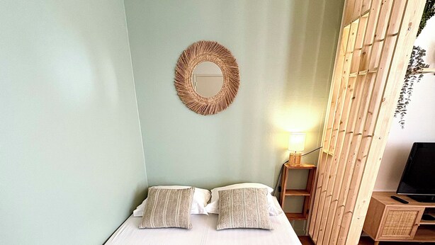 Uma cama de solteiro com colchão branco, duas almofadas e duas cobertas dobradas. Um criado-mudo de madeira com abajur fica ao lado da cama.