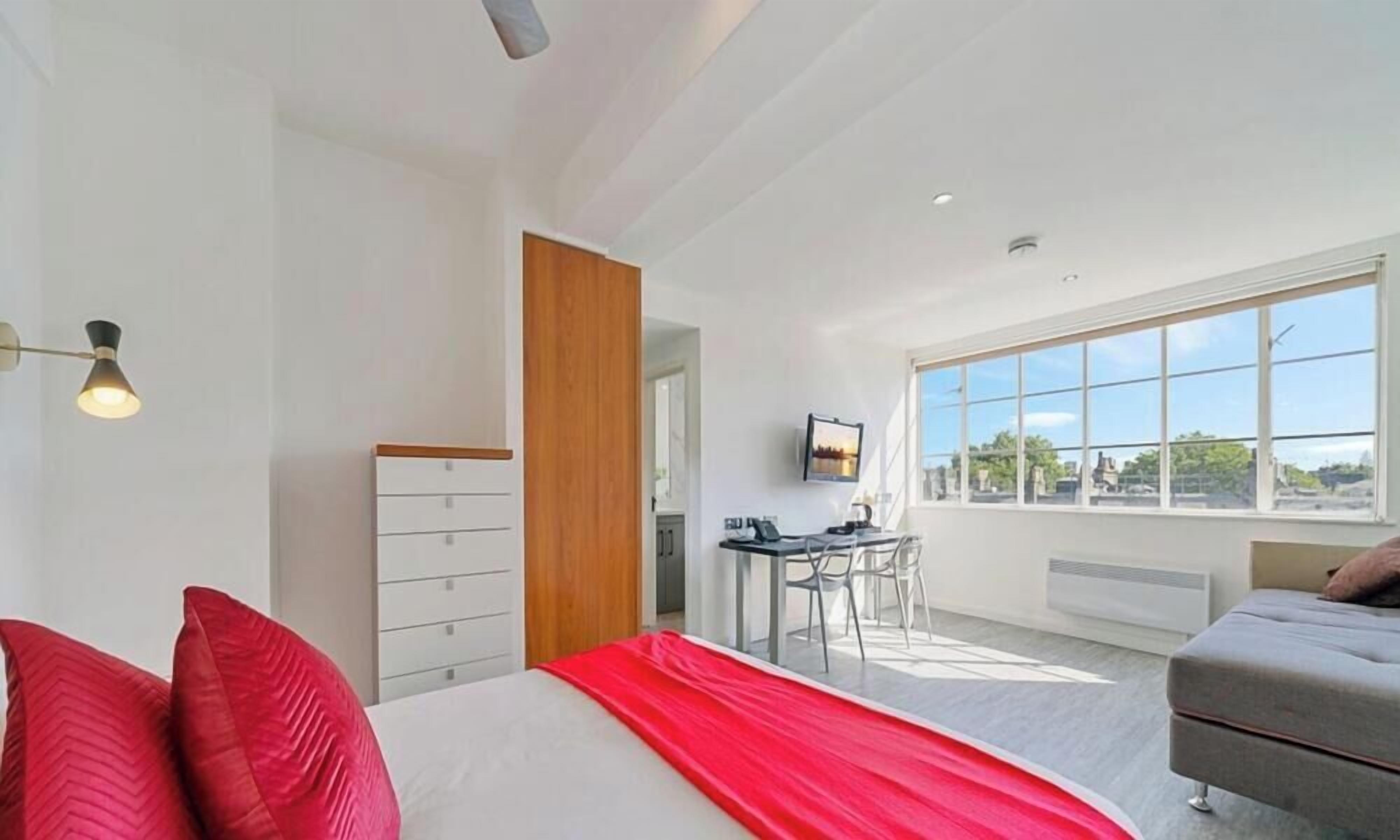 Une chambre d’hôtel moderne, équipée d’un lit, d’un bureau et offrant une vue sur la ville grâce à de grandes fenêtres.