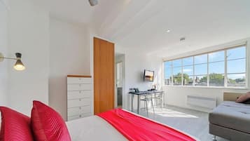 Une chambre d’hôtel moderne, équipée d’un lit, d’un bureau et offrant une vue sur la ville grâce à de grandes fenêtres.