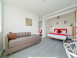 A modern hotel room with a sofa, a bed with red bedding, a mirror, and a ceiling fan. - Compact South Kensington Stay (London)