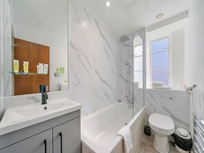 Ein modernes Badezimmer mit Marmorwand, einer Badewanne, einer Toilette und einer Dusche.