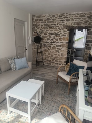 Ein Wohnzimmer mit Steinwand, einer Couch, einem Couchtisch, einem Sessel und einem Fernseher.