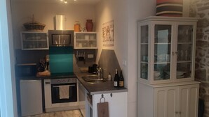 Een kleine keuken met een magnetron, oven en spoelbak. Er is een kast met glazen deuren en een kleine koelkast.