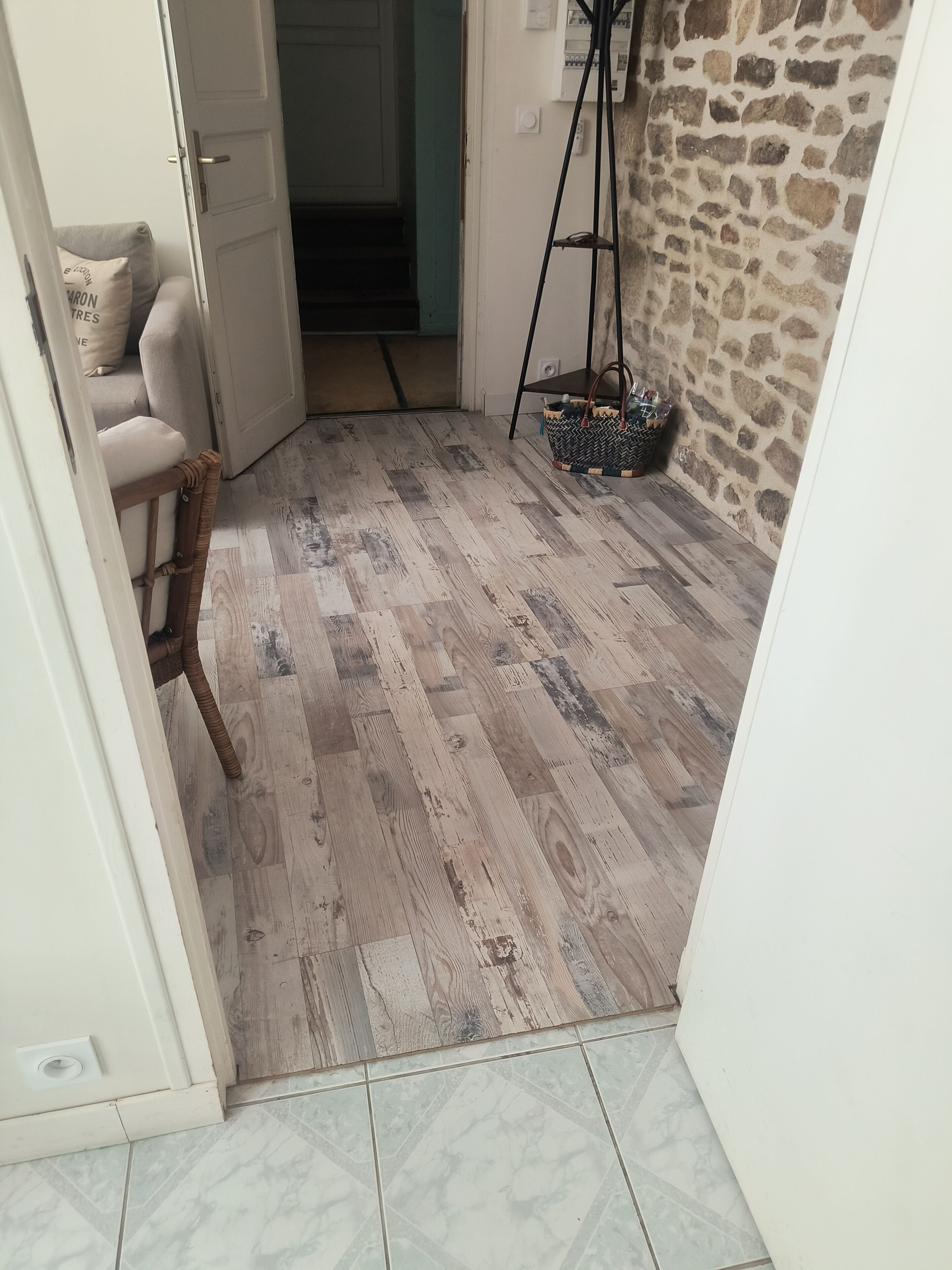 Une pièce avec un plancher en bois, un mur en pierre, une porte donnant sur une autre pièce et un lampadaire.