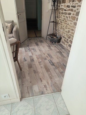 Ein Zimmer mit Holzboden, Steinwand, einer zurueckliegenden Raeumkuette und einer Stehlampe.