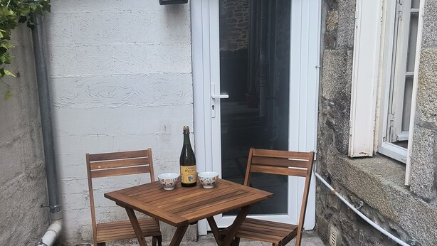 Een houten tafel met vier stoelen, een fles en een schaal op een betegeld terras.