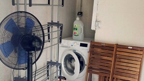 Een wasruimte met een wasmachine, een droogrek, een ventilator en een fles wasmiddel.