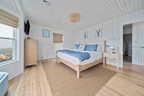 Ein Schlafzimmer mit einem großen Bett, Holzböden, einem Deckenventilator und Blick durch das Fenster.