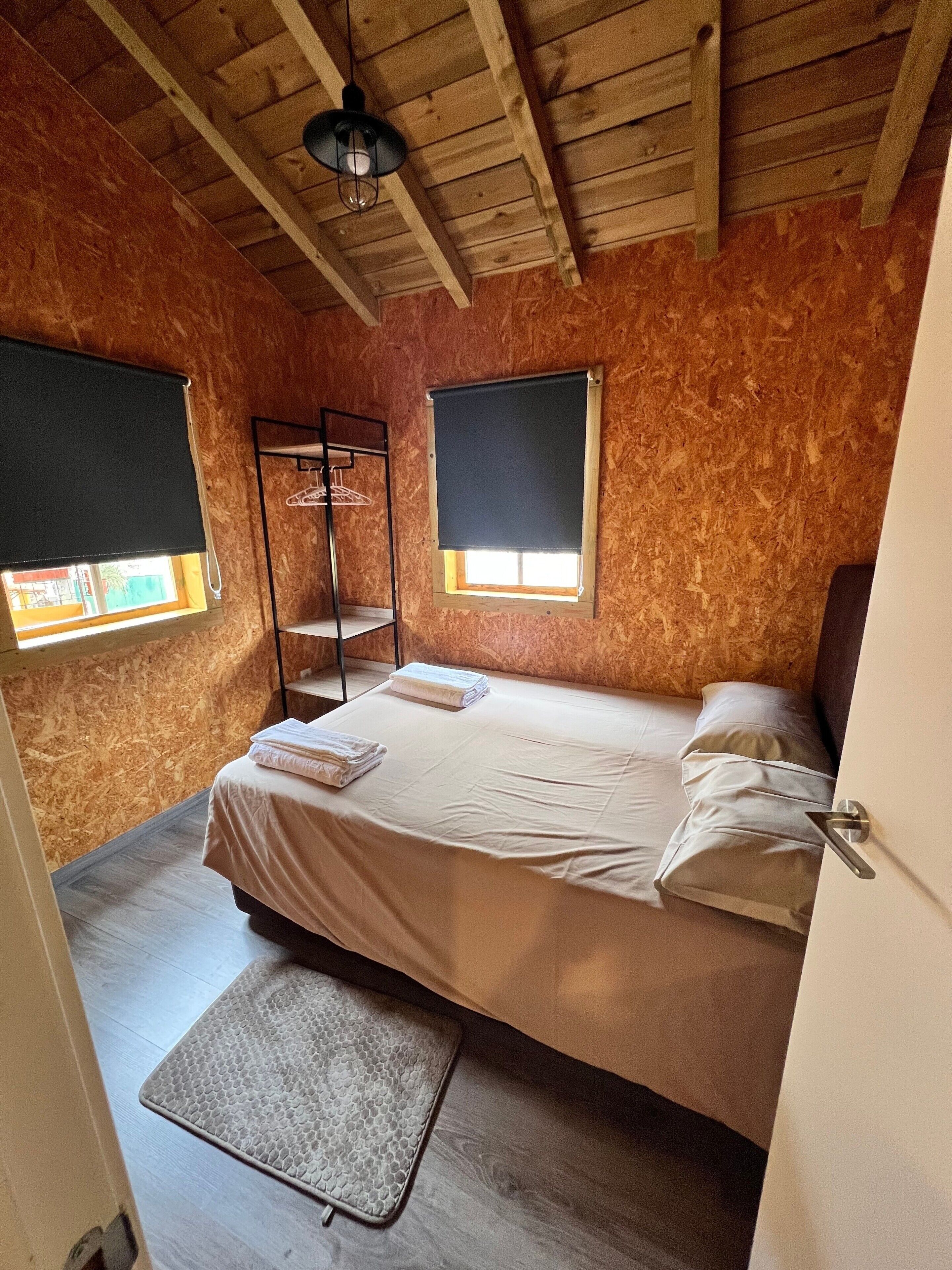 Een kamer met een bed, raam, kledingrek en een deur.