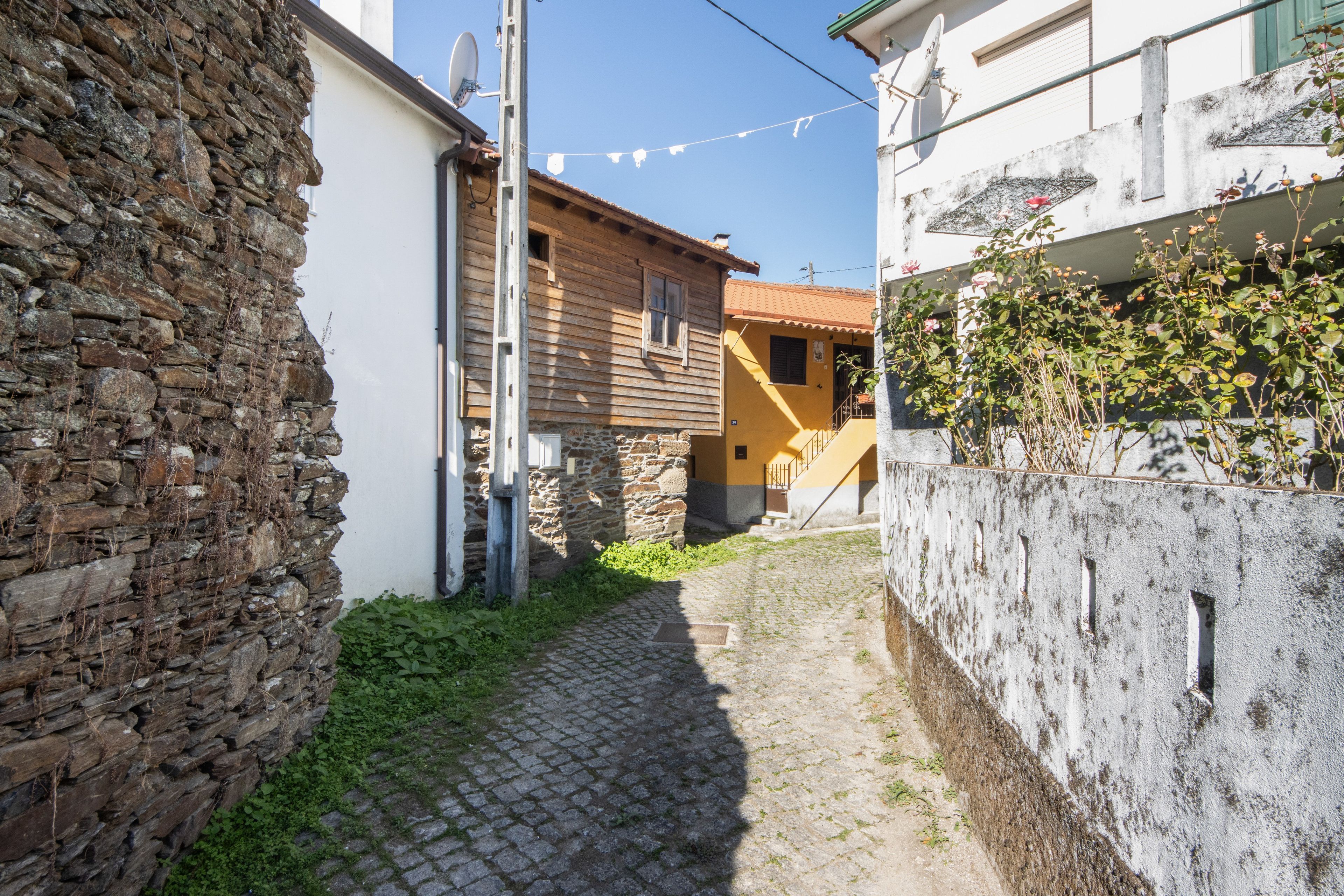 Un estrecho callejón adoquinado con muros de piedra a un lado y un edificio con fachada amarilla al otro.