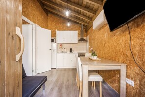 Cozinha compacta com armários brancos, teto de madeira e área de refeições com mesa e cadeiras.