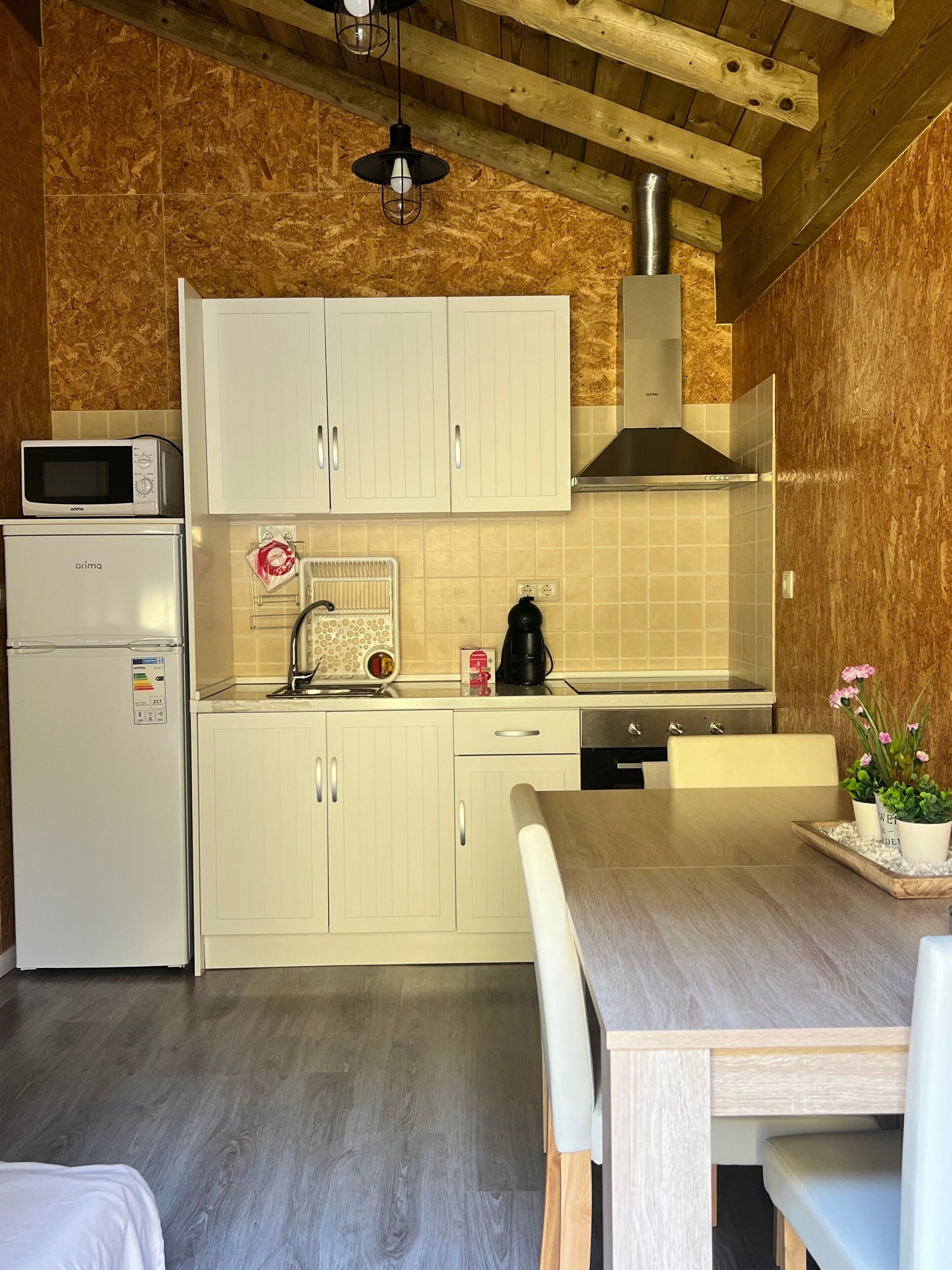 Una cucina compatta con mobili bianchi, un forno a microonde, una macchina da caffè e un lavello.