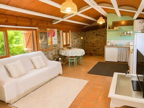 A cozy room with a white sofa, a dining table, and a kitchen area with a stone wall.