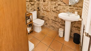 Un baño pequeño con pared de piedra, techo de madera, inodoro blanco, lavabo y espejo.
