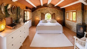 Un dormitorio con pared de piedra, vigas de madera en el techo, una cama, un aparador, un tocadiscos y un estufa de leña.
