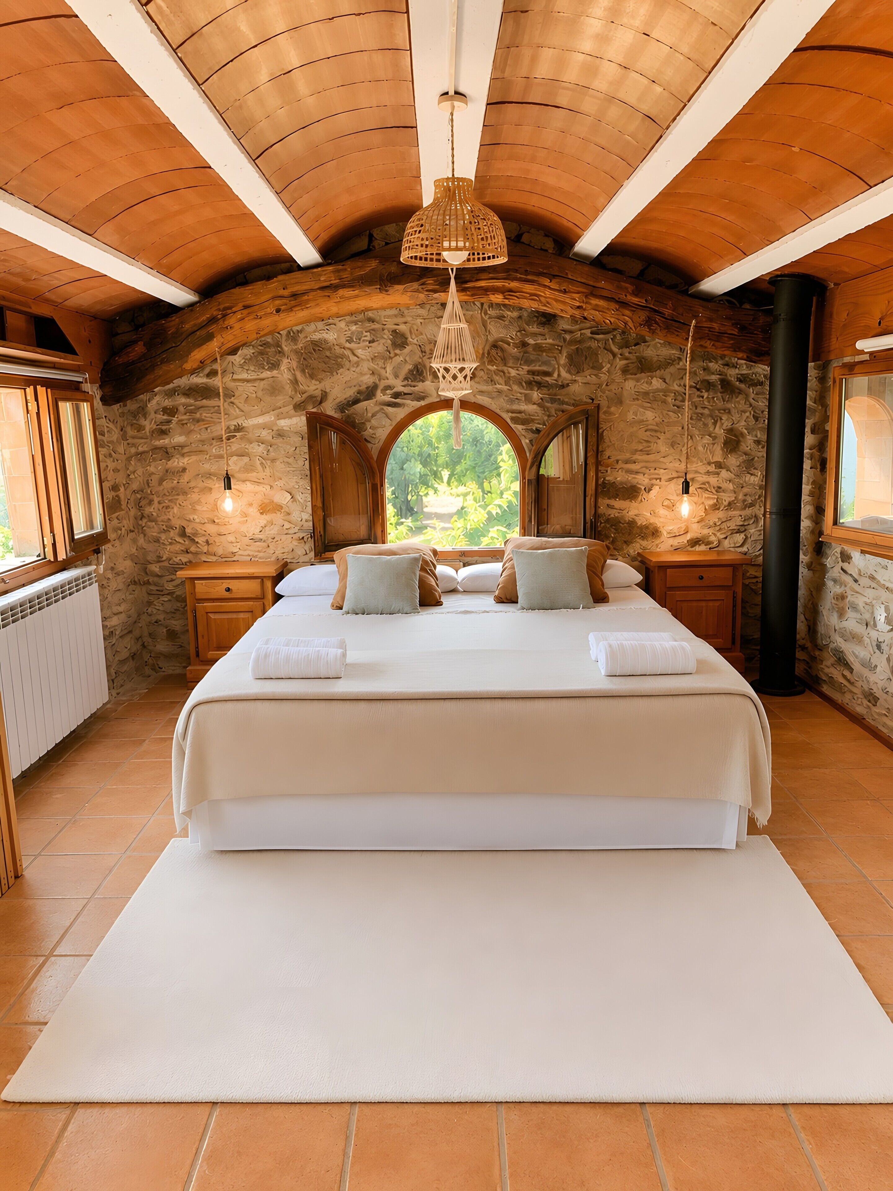 Un dormitorio con una cama grande, paredes de piedra, vigas de madera y vistas a través de una ventana.