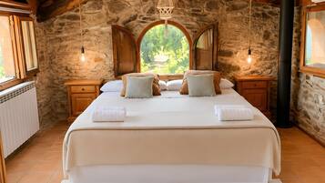 Un dormitorio con una cama grande, paredes de piedra, vigas de madera y vistas a través de una ventana.