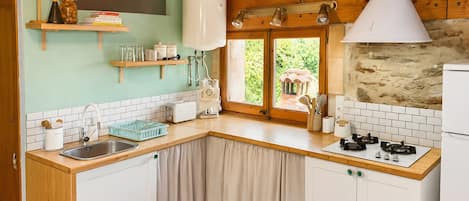Una cocina con armarios blancos, encimera de madera, estufa integrada y ventana con vista a la vegetación.