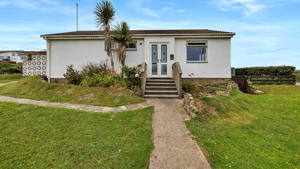 A single-story house with a front entrance, a small porch, and a pathway leading to the door. - Scenic Haven With Private Pond (Bude)