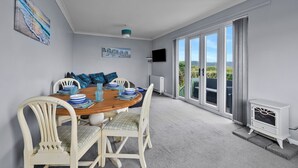 A dining area with a round table, white chairs, and a view through large sliding glass doors. - Scenic Haven With Private Pond (Bude)