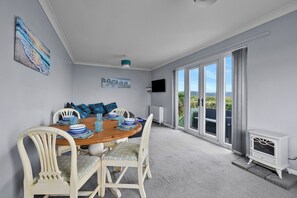A dining area with a round table, white chairs, and a view through large sliding glass doors. - Scenic Haven With Private Pond (Bude)