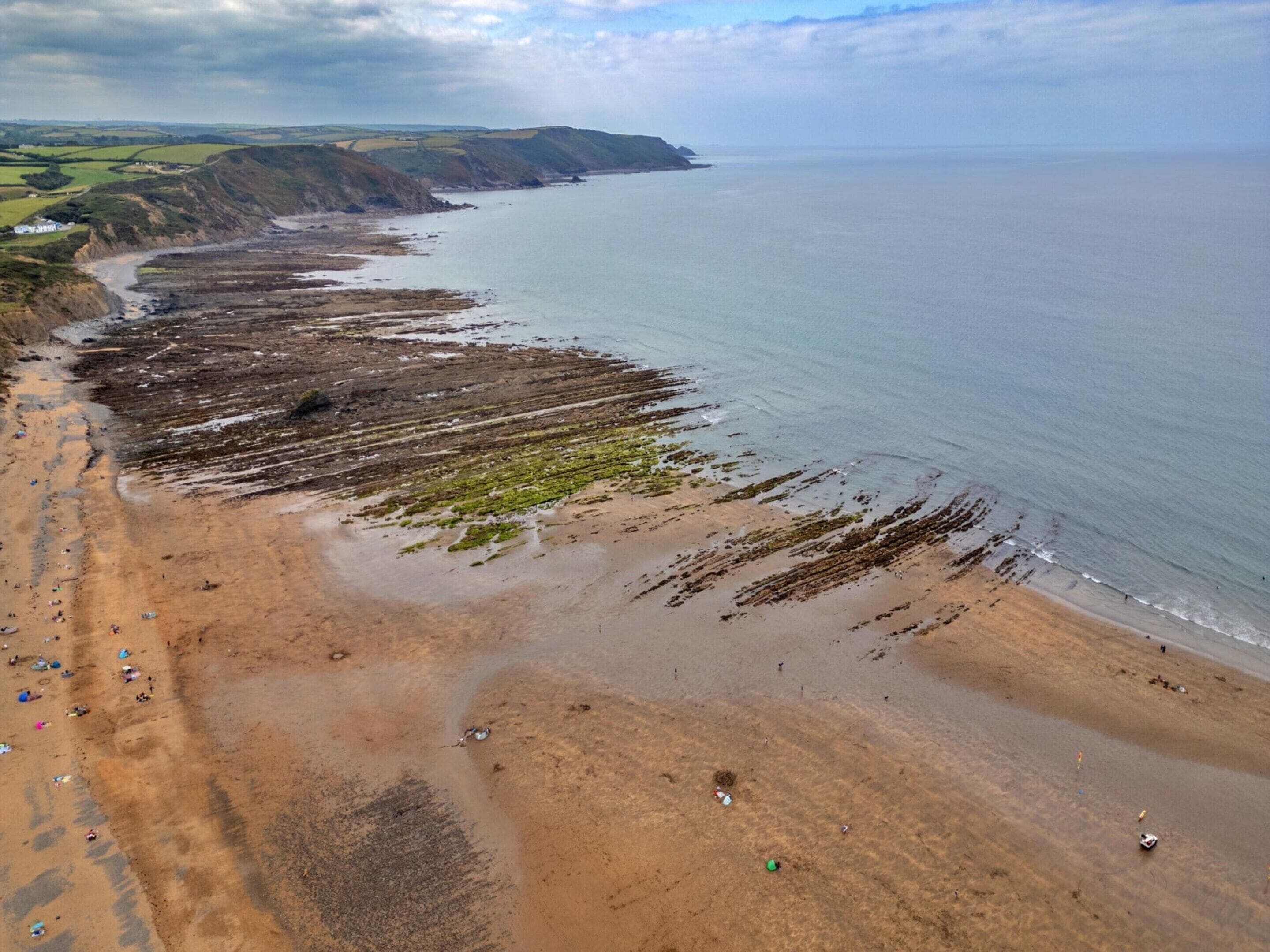 A coastal beach with a wide sandy area, a rocky shoreline, and a distant view of the sea.
