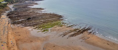 A coastal beach with a wide sandy area, a rocky shoreline, and a distant view of the sea.