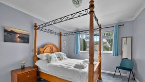 A four-poster bed with a wooden headboard, a bedside table with drawers, a chair, and a window with curtains. - Scenic Haven With Private Pond (Bude)
