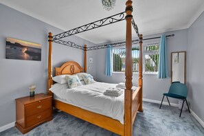 A four-poster bed with a wooden headboard, a bedside table with drawers, a chair, and a window with curtains. - Scenic Haven With Private Pond (Bude)