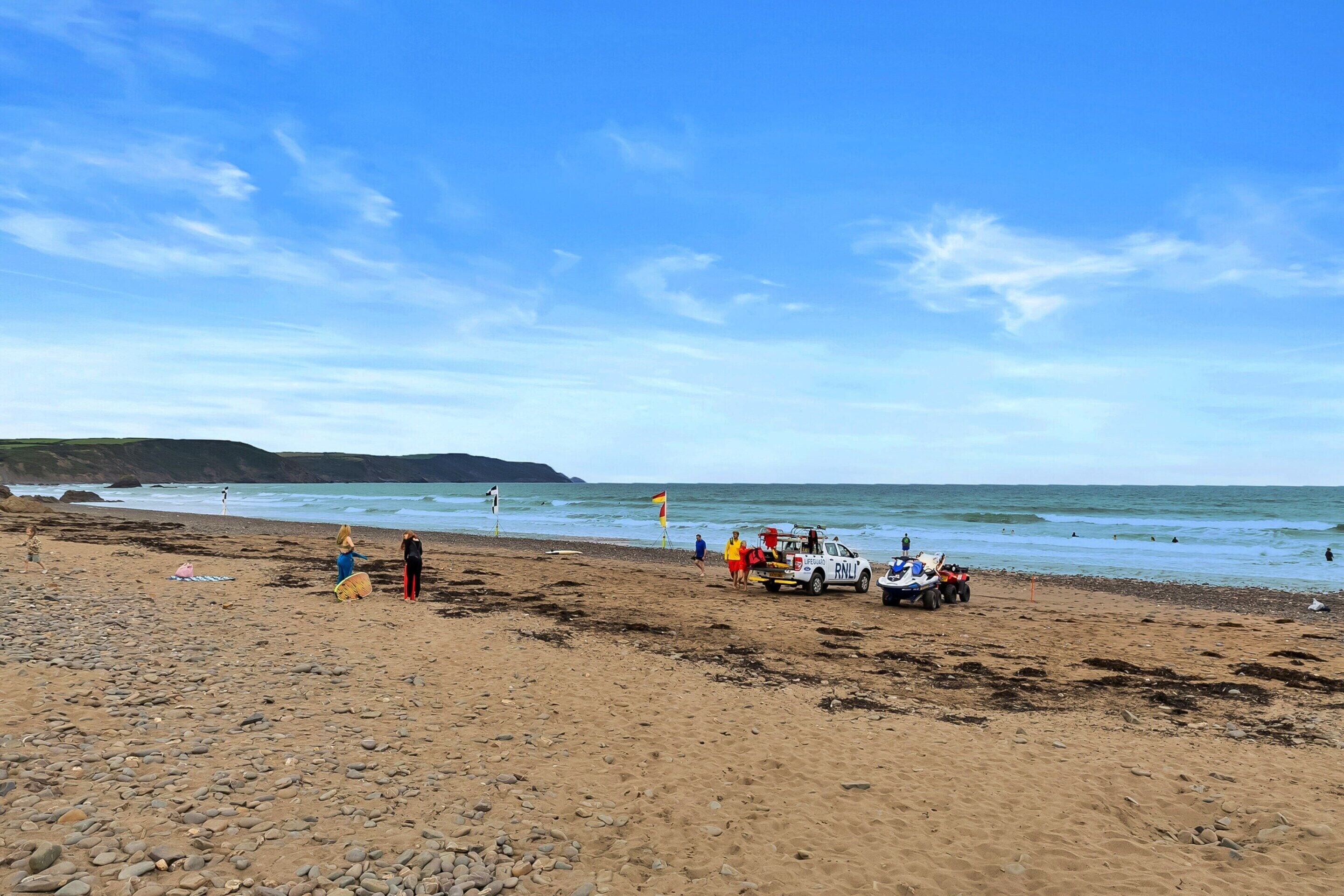 Une plage avec un poste de surveillance des sauveteurs, un véhicule tout-terrain et des gens qui se promènent le long du rivage.