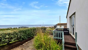 A seaside property with a view of the ocean, a wooden deck, and a white building. - Scenic Haven With Private Pond (Bude)