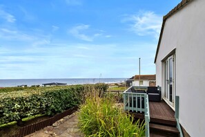 A seaside property with a view of the ocean, a wooden deck, and a white building. - Scenic Haven With Private Pond (Bude)