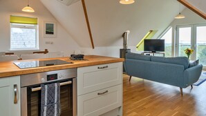 A modern kitchen with a built-in oven, a dining area with a table and chairs, a grey sofa, and a television in a corner. - Stunning Broad Haven Beach House (Newquay)