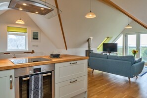 Eine moderne Küche mit Einbauofen, eine Essecke mit Tisch und Stühlen, ein graues Sofa und ein Fernseher in einer Ecke.